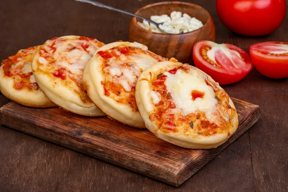 Mini Cheese Pizza Mini cheese pizzas topped with tomato sauce and melted cheese on a wooden board.
