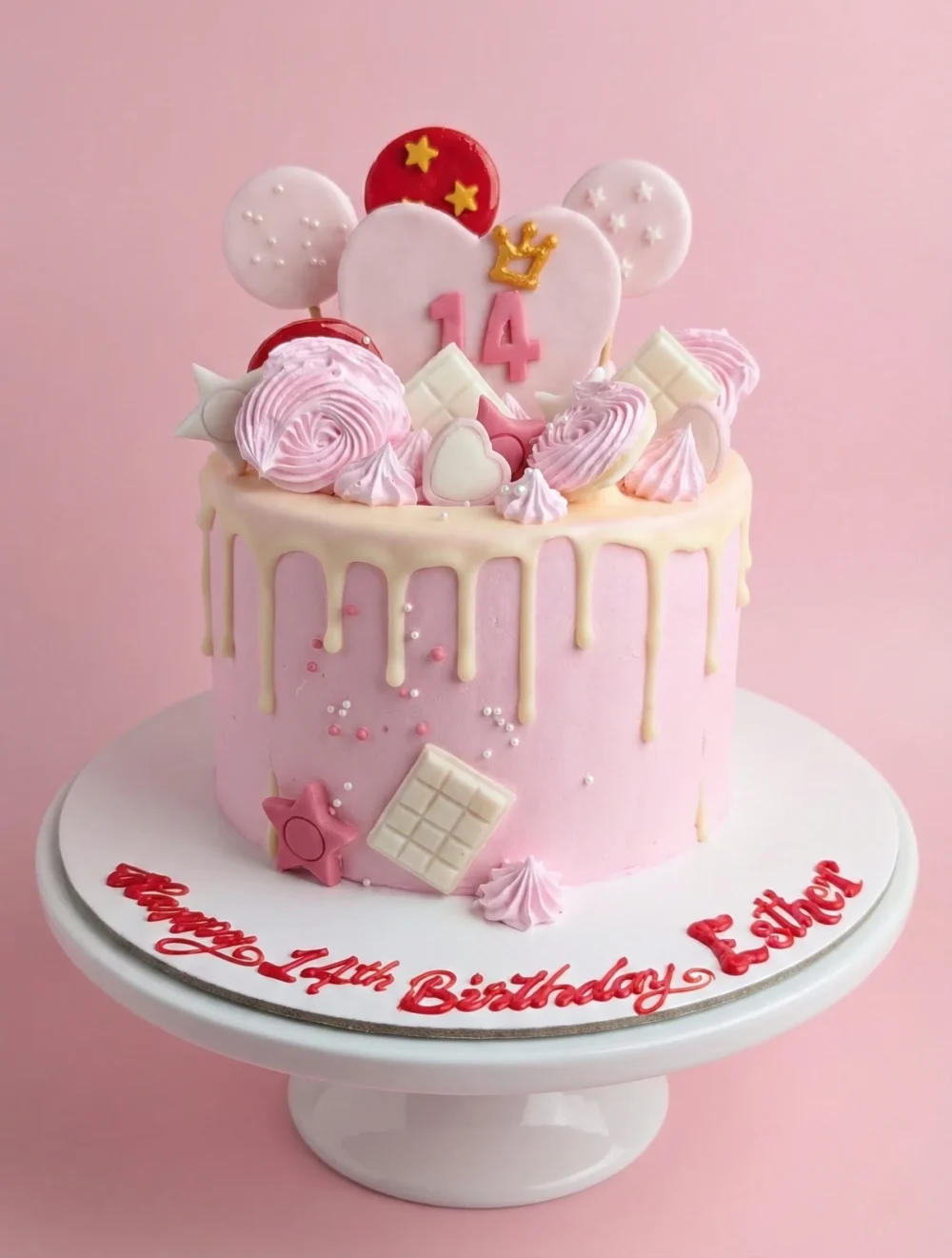 Pink and White Drip Cake - Dubai Pastel pink drip birthday cake for 14th birthday featuring white chocolate drip, pink meringue swirls, chocolate squares, and a heart-shaped topper with a gold crown. Cake board reads Happy 14th Birthday Esther in red script.